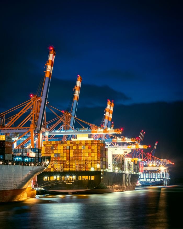 who-we-are Vibrant night view of container ships at Hamburg port with cranes illuminated.