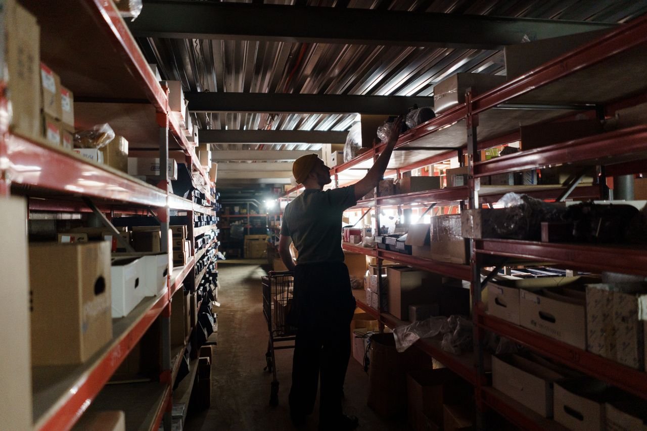 why-choose-us A worker arranging inventory on shelves in a dimly lit warehouse, utilizing efficient storage practices.
